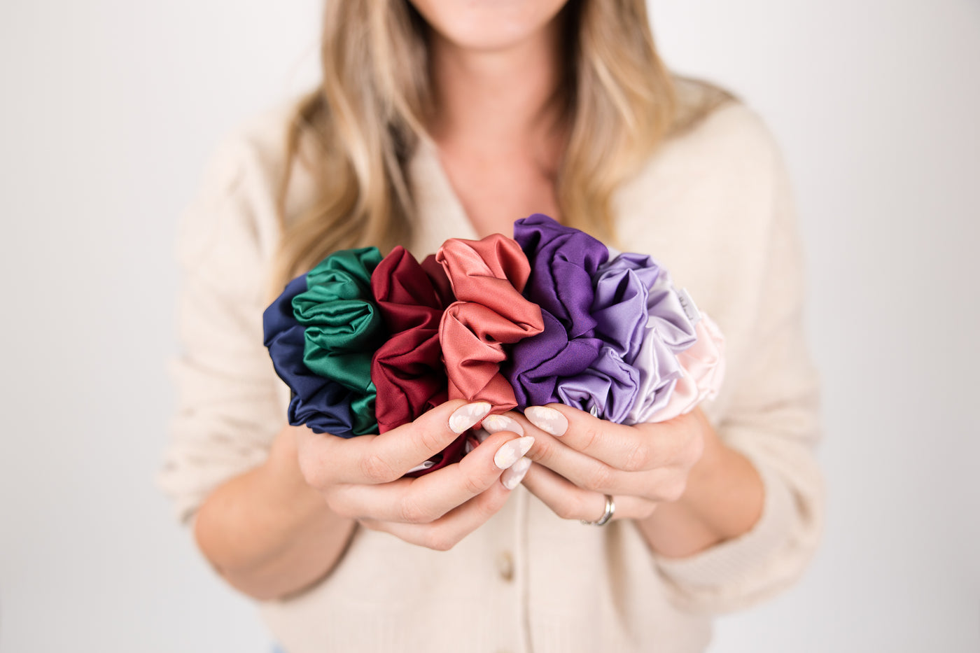 Woman holding colorful scrunchies against a plain background